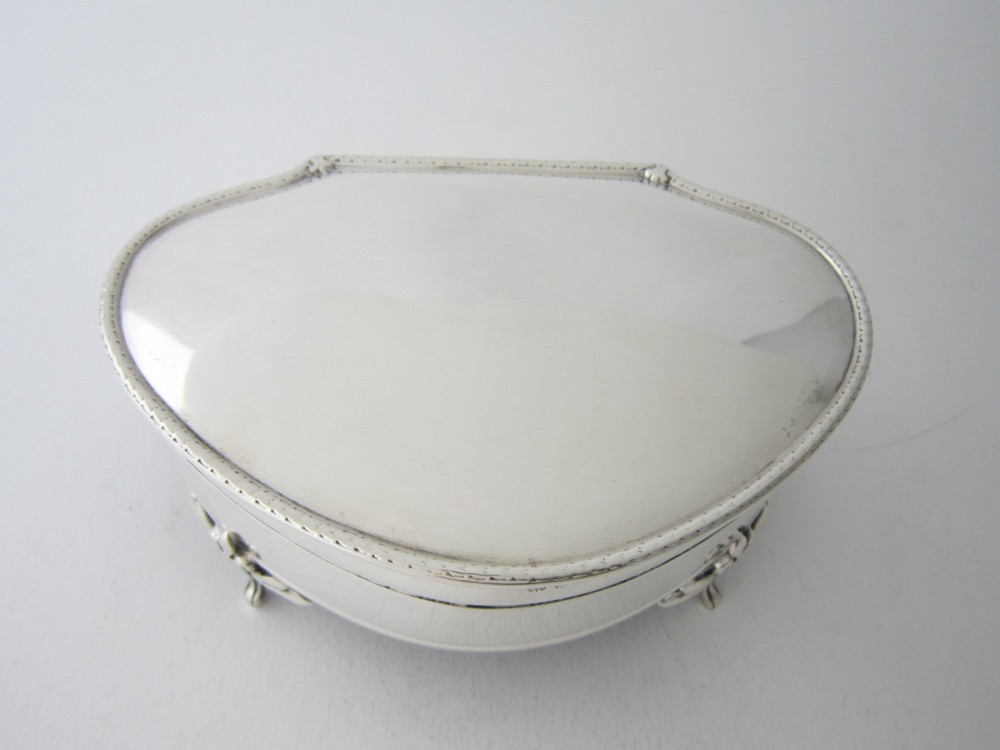 A kidney-shaped antique sterling silver trinket box with a beaded edge hinged lid standing on small decorative feet.