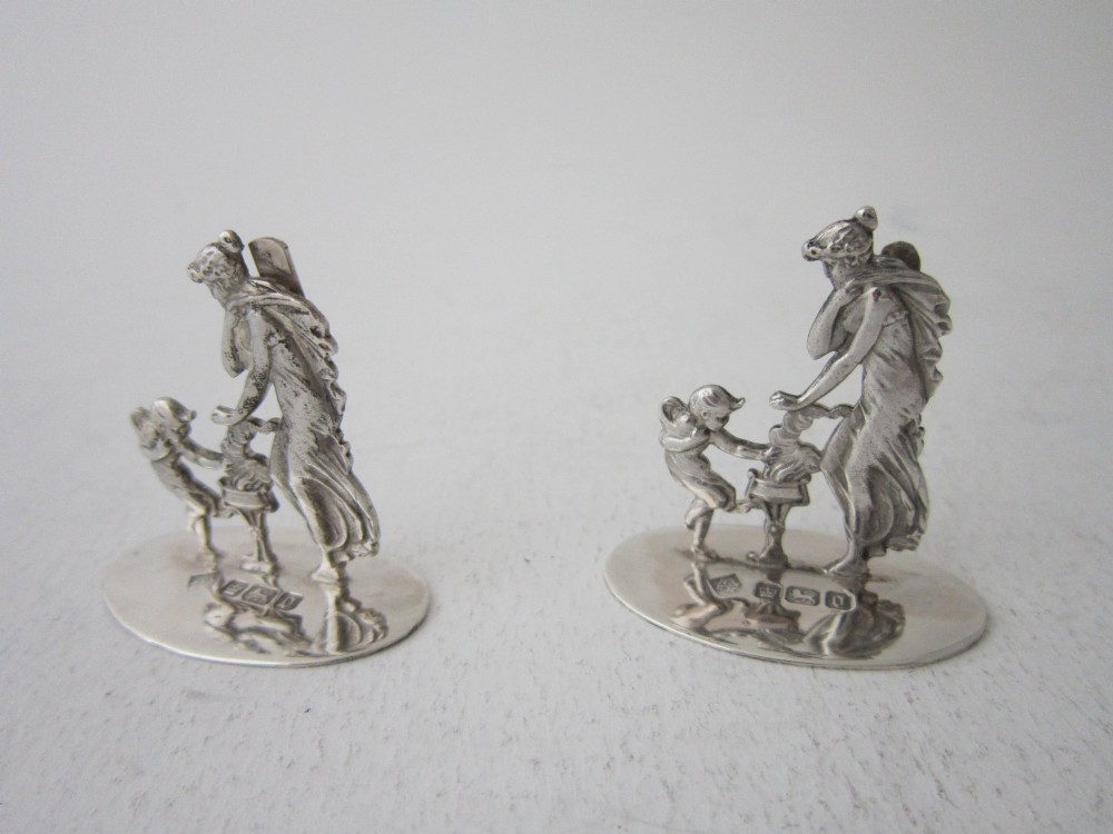 A pair of Edwardian sterling silver place card holders featuring classical female figures and cherubs on round hallmarked bases. View II