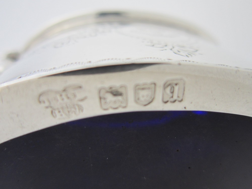 An antique George V sterling silver mustard pot featuring intricate garland engraving, a hinged lid, C-scroll handle, and an included silver spoon. View XI
