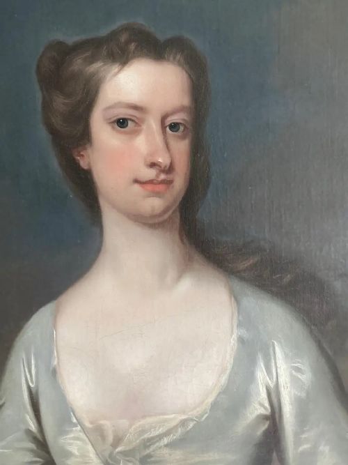 fig 1. An 18th-century three-quarter-length oil portrait of a woman in an ivory silk gown holding a sprig of small white flowers, set inside a carved gold gilt frame.