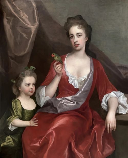 fig 1. An oil painting depicting a seated woman in a crimson gown holding a small green bird alongside a child in a green dress, encased in a carved gold frame.