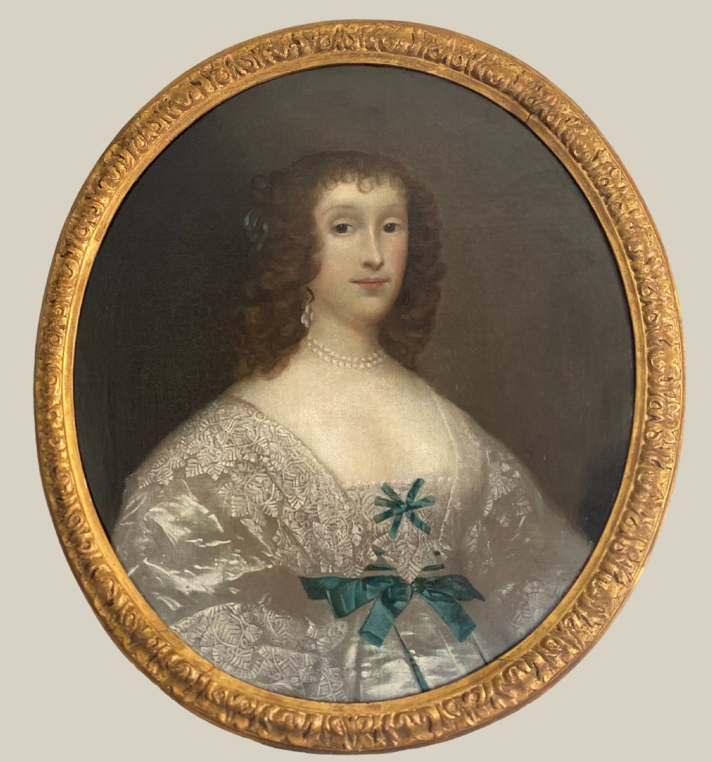 An oval seventeenth-century oil portrait of a lady with dark curly hair wearing a lace dress and pearl jewellery inside a carved gold frame.