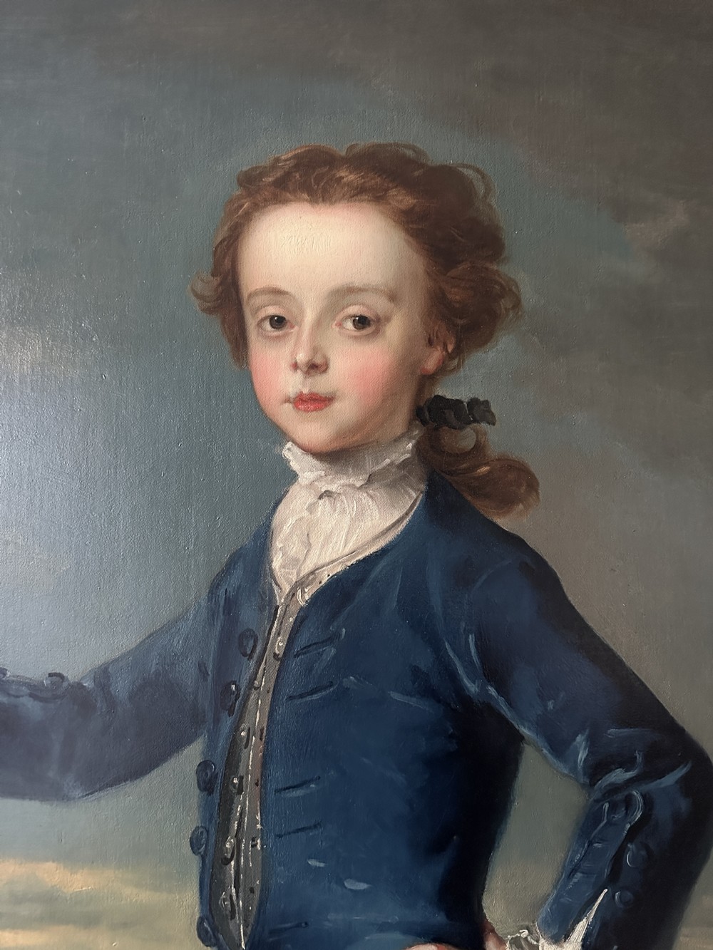 An 18th-century full-length oil painting of a young boy in a blue coat holding a whip beside a spinning top, set within a carved gold frame. View IV