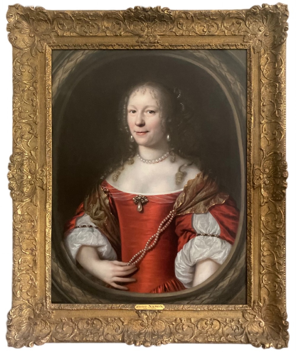 An oil portrait of a lady in a red dress with pearl jewellery set inside a carved giltwood frame.