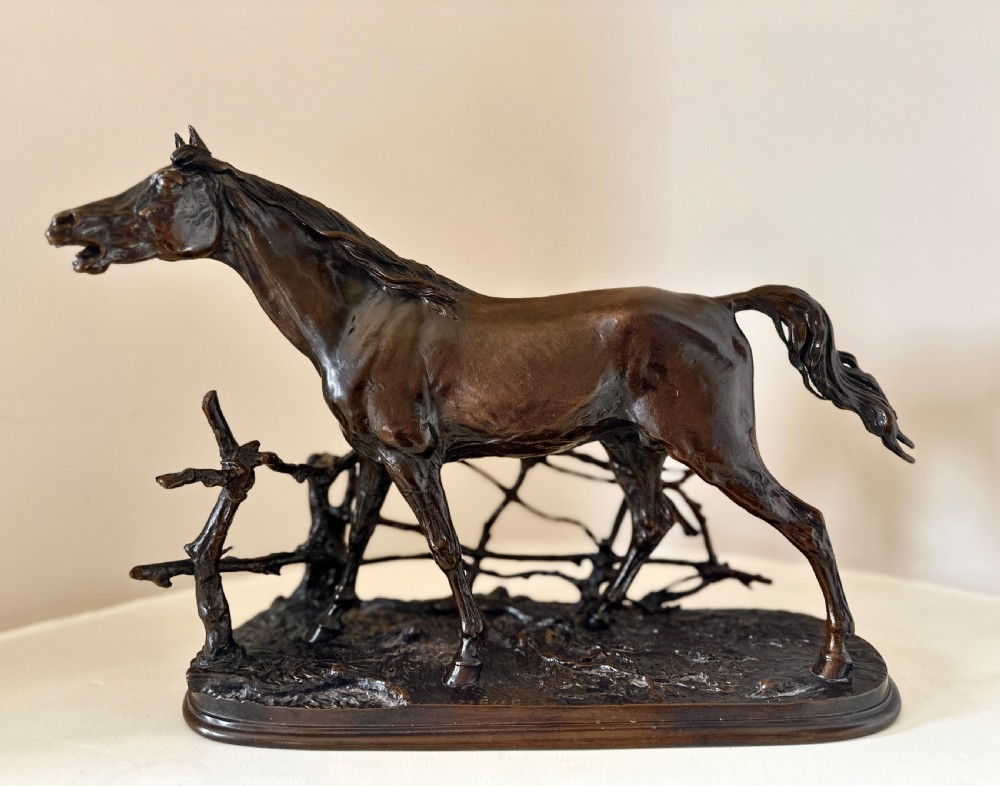 A dark brown 19th-century bronze sculpture of a horse stepping over a wooden hurdle fence mounted on an oval bronze base.
