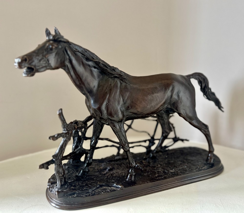 A dark brown 19th-century bronze sculpture of a horse stepping over a wooden hurdle fence mounted on an oval bronze base. View II