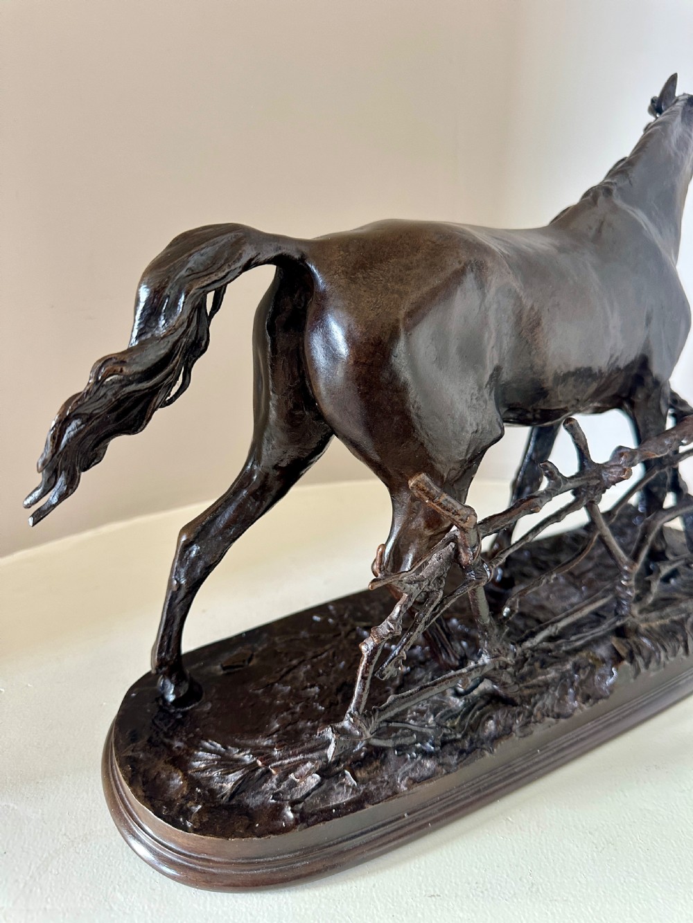 A dark brown 19th-century bronze sculpture of a horse stepping over a wooden hurdle fence mounted on an oval bronze base. View III
