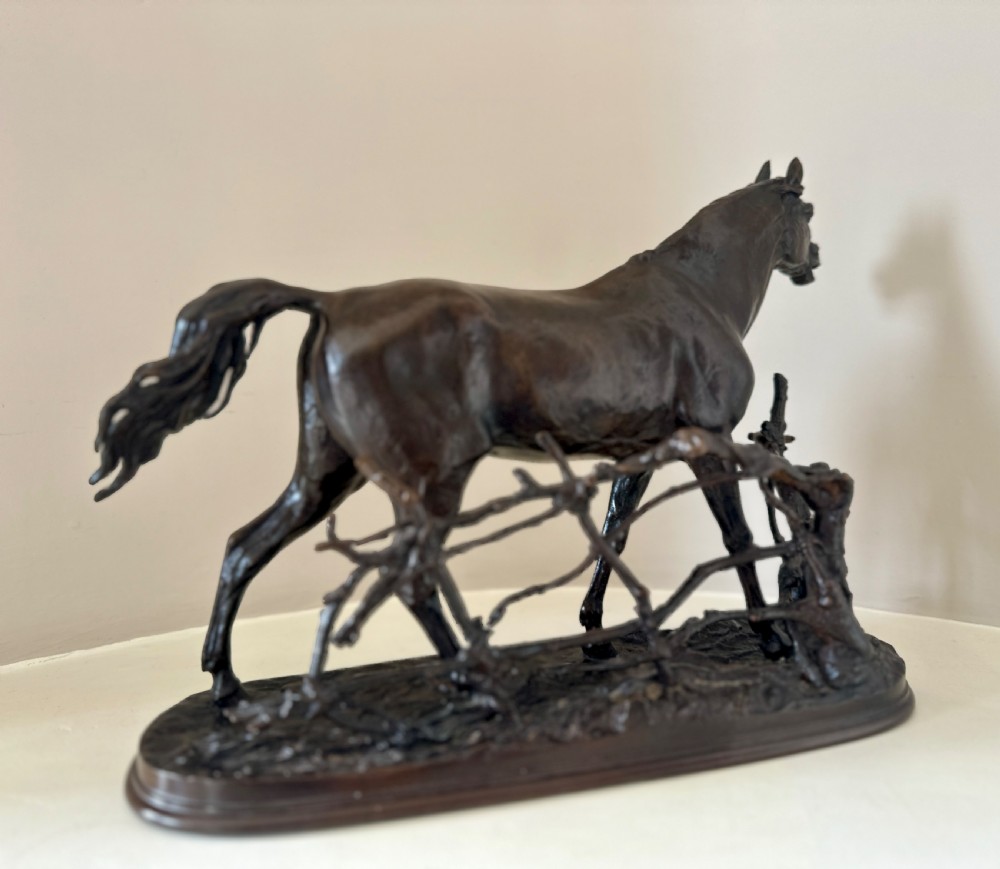 A dark brown 19th-century bronze sculpture of a horse stepping over a wooden hurdle fence mounted on an oval bronze base. View IV
