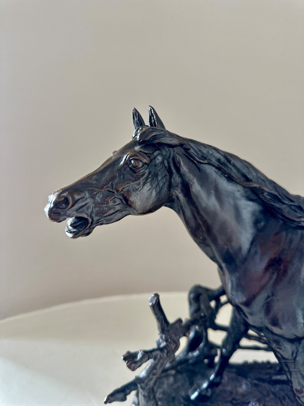 A dark brown 19th-century bronze sculpture of a horse stepping over a wooden hurdle fence mounted on an oval bronze base. View VI