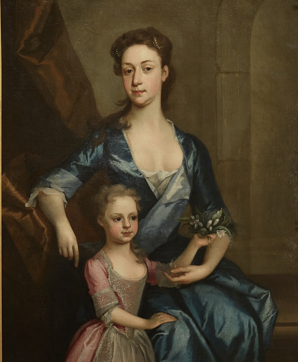 An eighteenth-century oil painting depicting a seated woman in a blue dress with a young child in a pink dress, presented within a carved gilt frame. View II