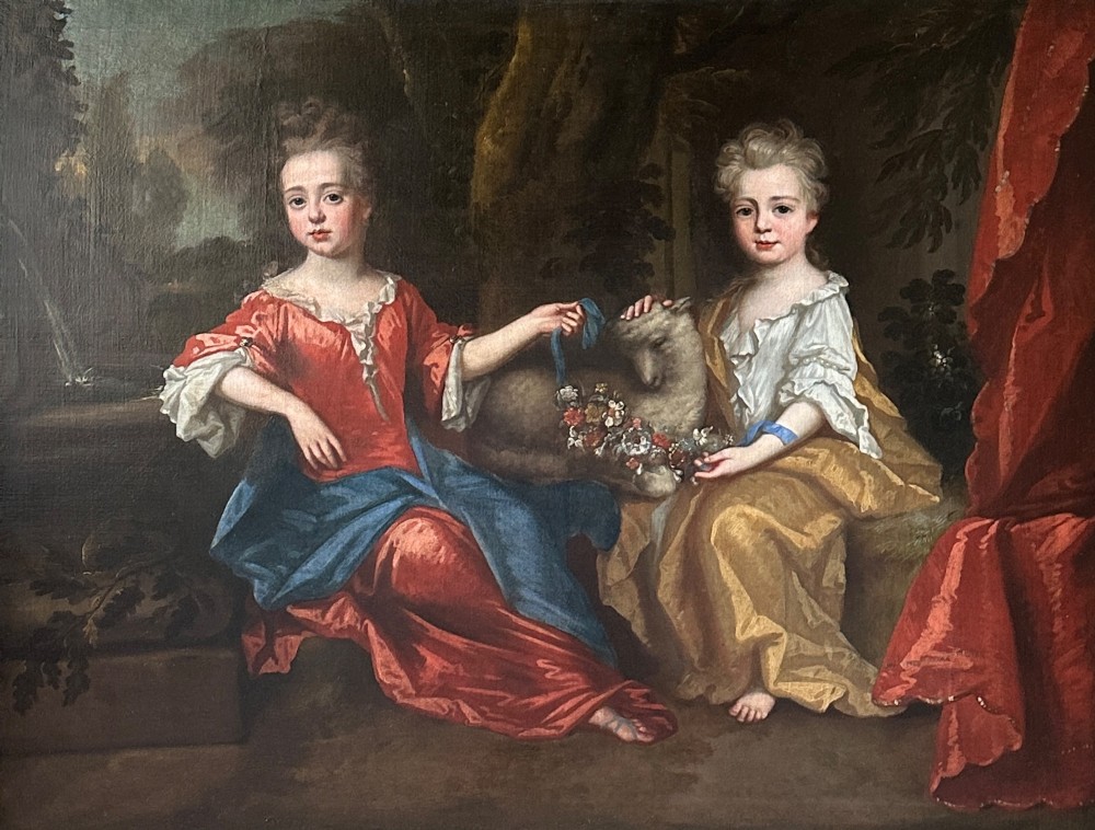 An 18th-century oil painting depicting two young girls seated in a natural landscape with a lamb, presented within an ornate carved giltwood frame. View II