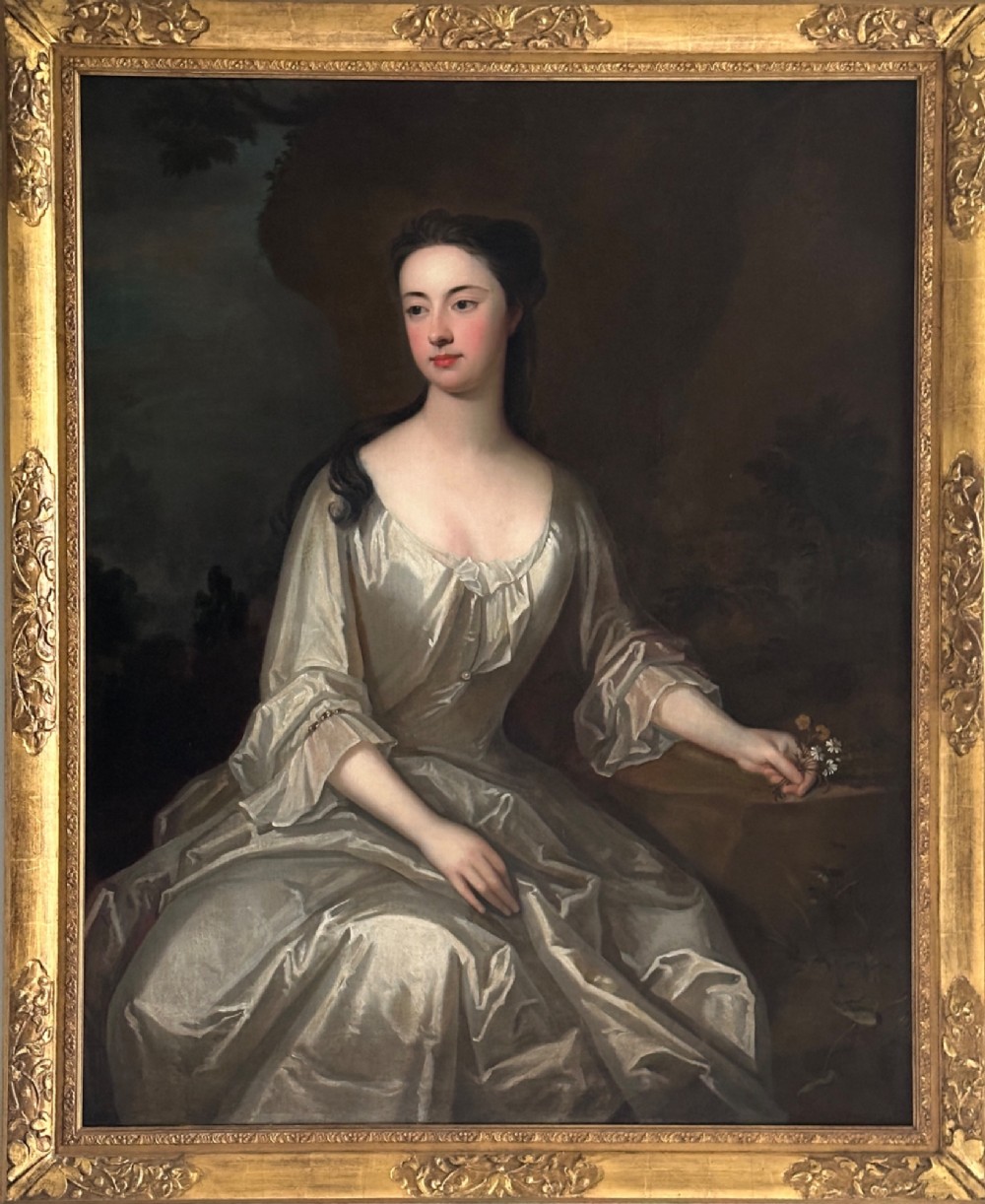 An early eighteenth-century oil painting on canvas depicting a seated lady in a silk gown within a carved giltwood frame.