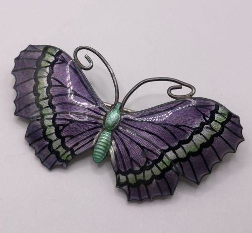 fig 1. A silver butterfly brooch featuring purple and green guilloche enamel wings with black details and coiled wire antennae.