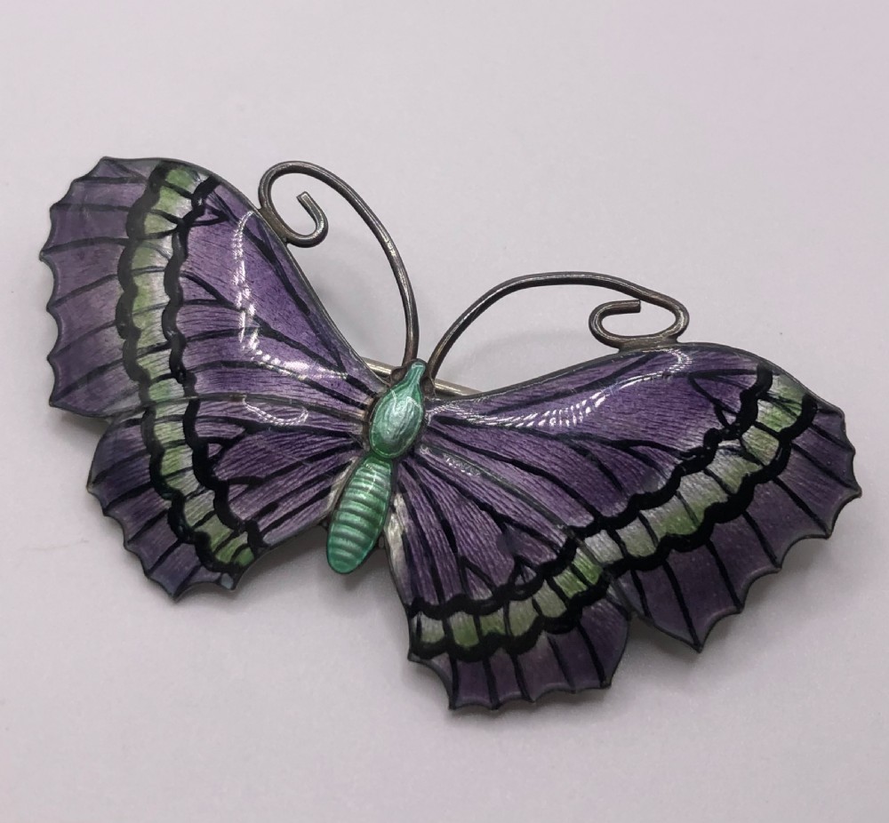 A silver butterfly brooch featuring purple and green guilloche enamel wings with black details and coiled wire antennae. View II