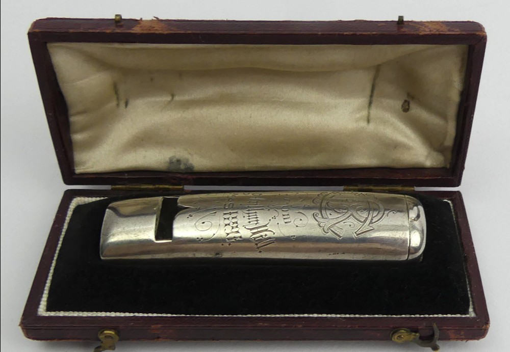 An engraved silver novelty whistle vesta case displayed inside a maroon velvet-lined presentation box.