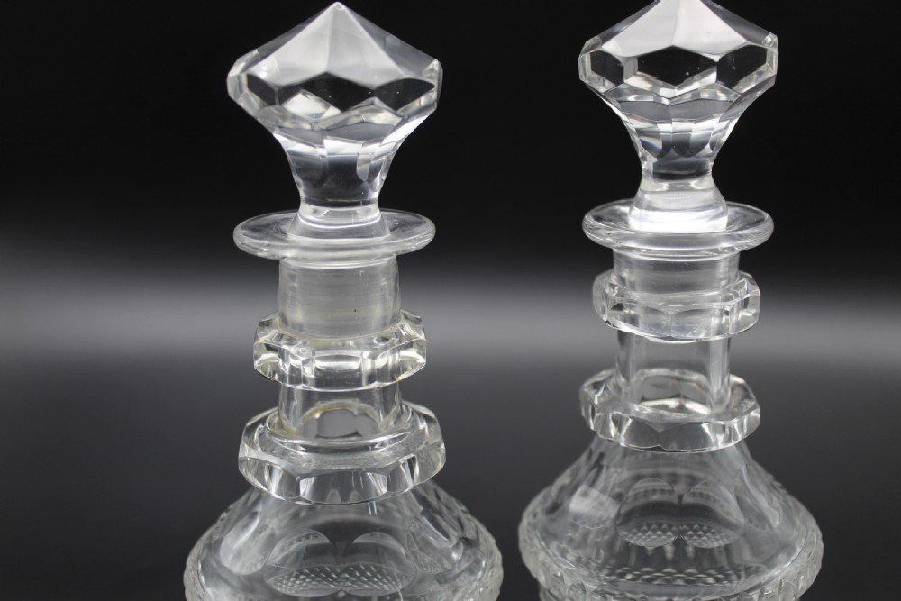 A pair of 19th-century clear cut glass decanters featuring three applied neck rings, geometric diamond cutting, and faceted stoppers. View II