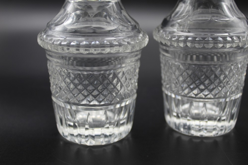 A pair of 19th-century clear cut glass decanters featuring three applied neck rings, geometric diamond cutting, and faceted stoppers. View III