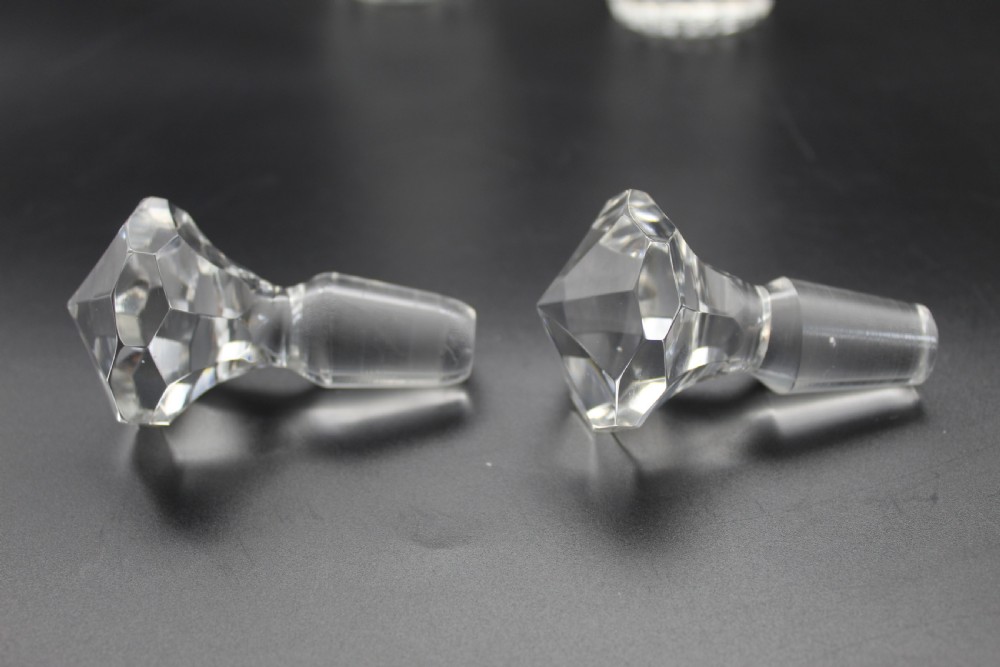 A pair of 19th-century clear cut glass decanters featuring three applied neck rings, geometric diamond cutting, and faceted stoppers. View V