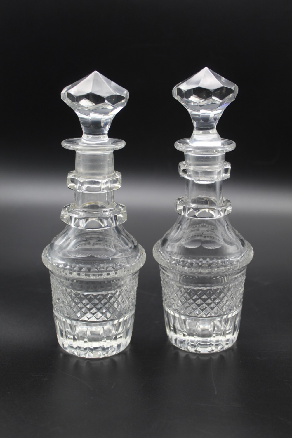 A pair of 19th-century clear cut glass decanters featuring three applied neck rings, geometric diamond cutting, and faceted stoppers.