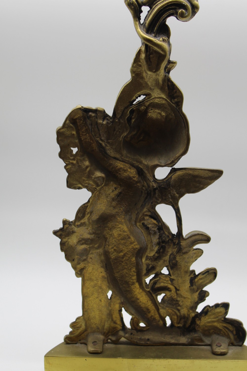 A Victorian cast brass doorstop featuring a standing winged cherub amidst acanthus leaf scrolls topped with a curved carrying handle. View V