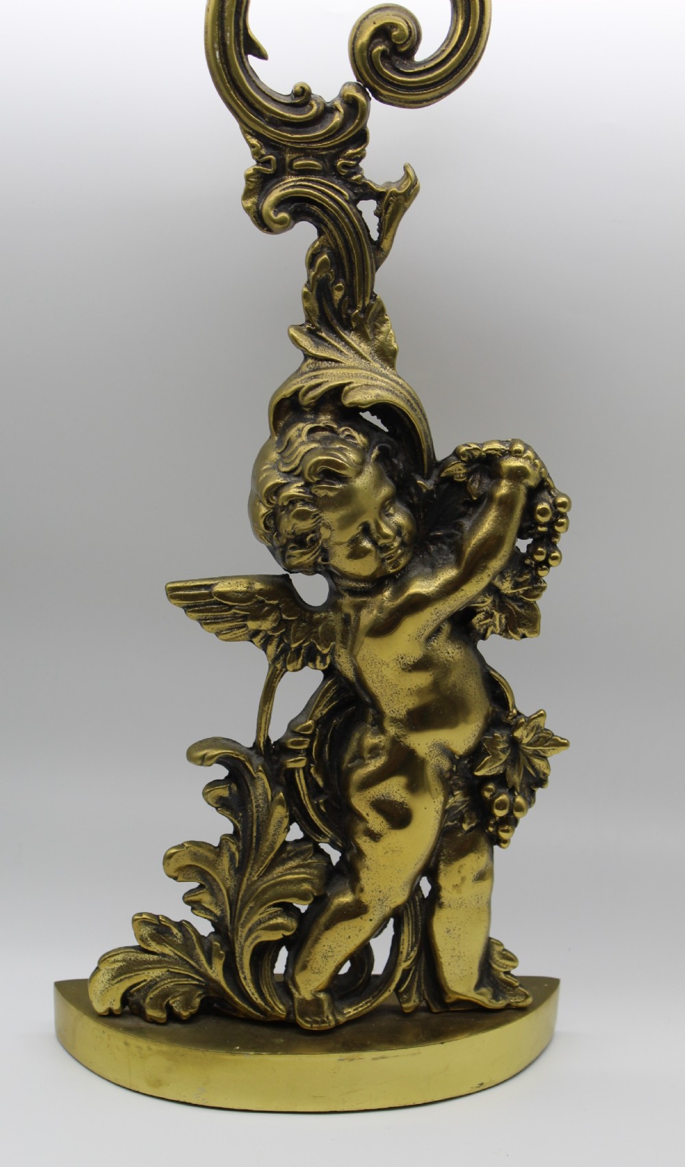 A Victorian cast brass doorstop featuring a standing winged cherub amidst acanthus leaf scrolls topped with a curved carrying handle. View VII
