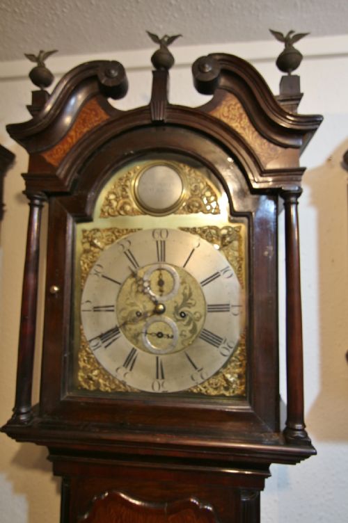 fig 1. An 18th-century oak and mahogany longcase clock featuring a brass dial, swan-neck pediment, and brass eagle finials.