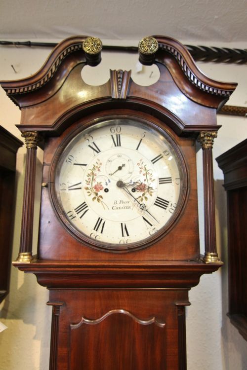 fig 1. A Georgian mahogany longcase clock featuring a swan-neck pediment, a round painted dial with Roman numerals, reeded columns, and central oval inlay on the trunk door.