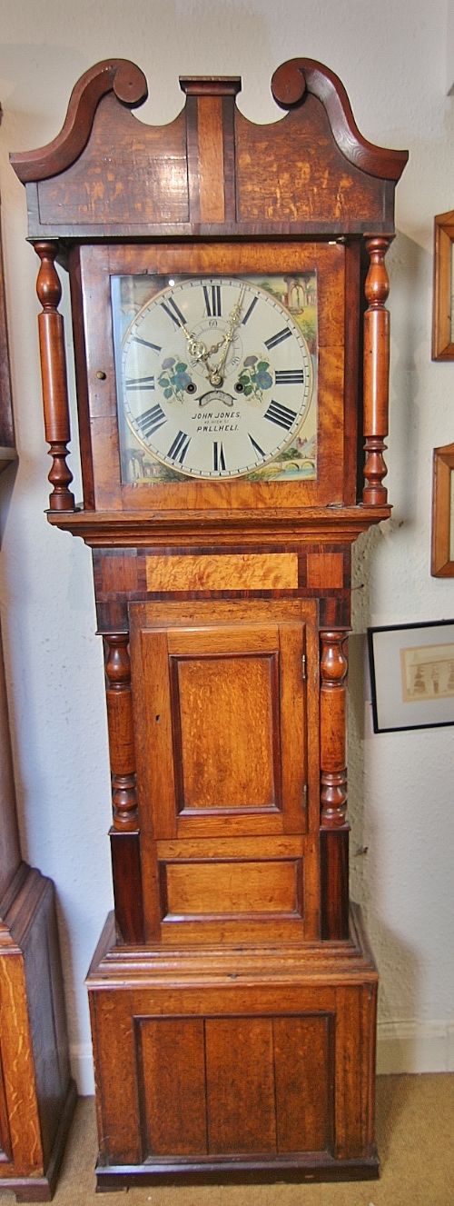 An antique Welsh oak and mahogany inlaid longcase clock featuring a swan-neck pediment, turned columns, and a painted dial signed John Jones Pwllheli.
