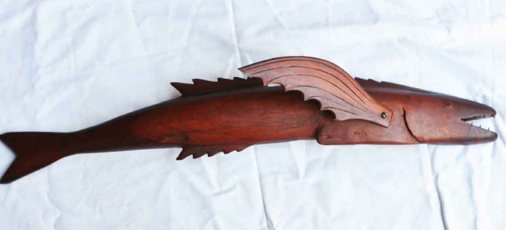 A late nineteenth-century hand-carved dark wood flying fish sculpture displaying carved wing-like pectoral fins and incised mouth details against a plain fabric background.
