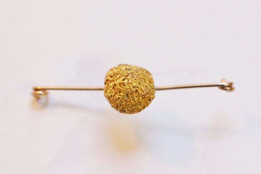 A 19th-century gold bar brooch featuring a central textured raw gold nugget mounted on a slender yellow gold pin stem.