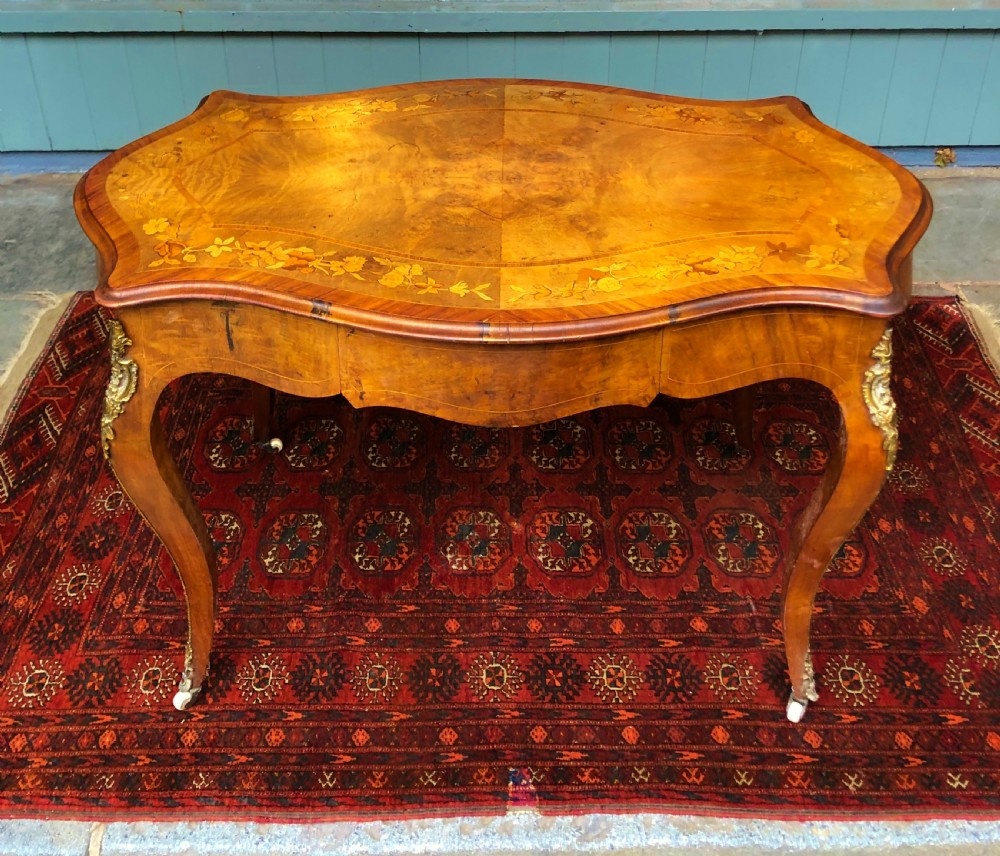 A 19th-century French Louis XV style inlaid writing desk featuring floral marquetry, a serpentine top, cabriole legs, and gilt-bronze mounts.