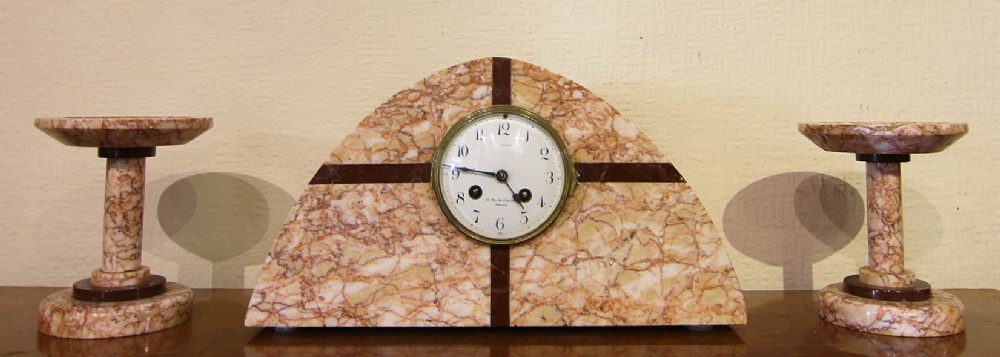 An Art Deco clock set featuring an arched central marble timepiece with dark geometric inlays flanked by two matching marble side garnitures.