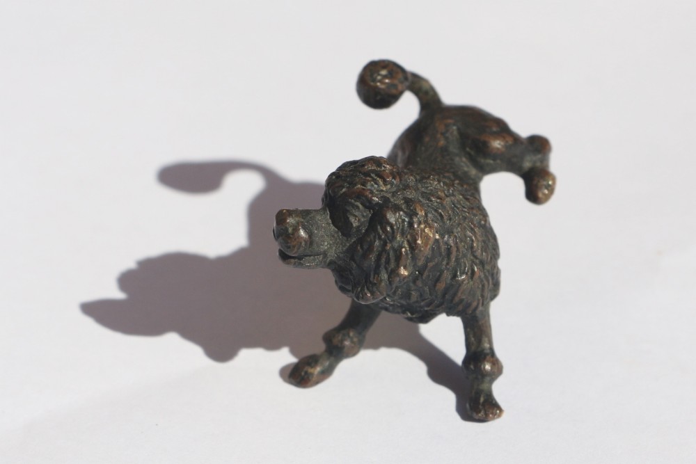 A late 19th-century dark patinated bronze miniature figurine of a clipped poodle depicted with one hind leg raised.