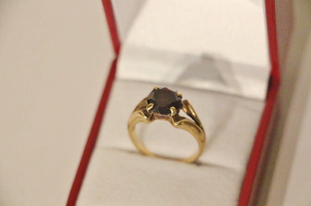 A 9ct yellow gold ring featuring a central dark red faceted gemstone mounted in a claw setting with split shoulders.