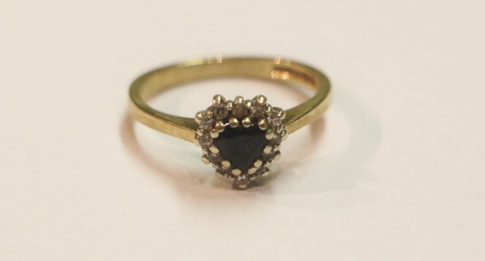A 9ct yellow gold ring featuring a central heart-shaped dark blue sapphire encircled by a halo of small diamonds.