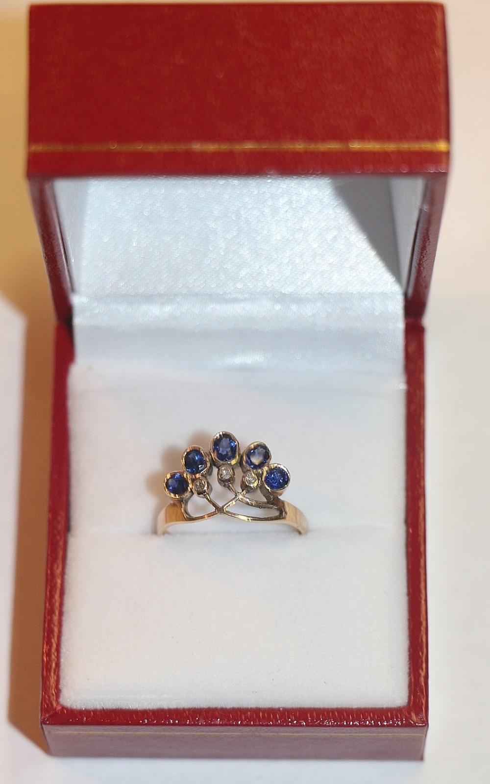 A 14ct yellow gold ring shaped like a tiara, featuring five claw-set blue sapphires and small diamond accents.