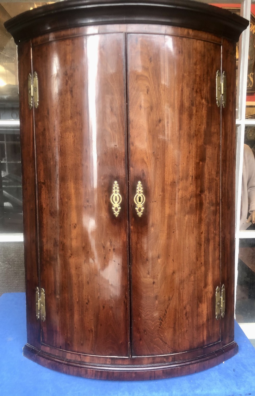 A Georgian bow-fronted mahogany corner cupboard with double doors, brass keyhole escutcheons, and visible brass hinges.