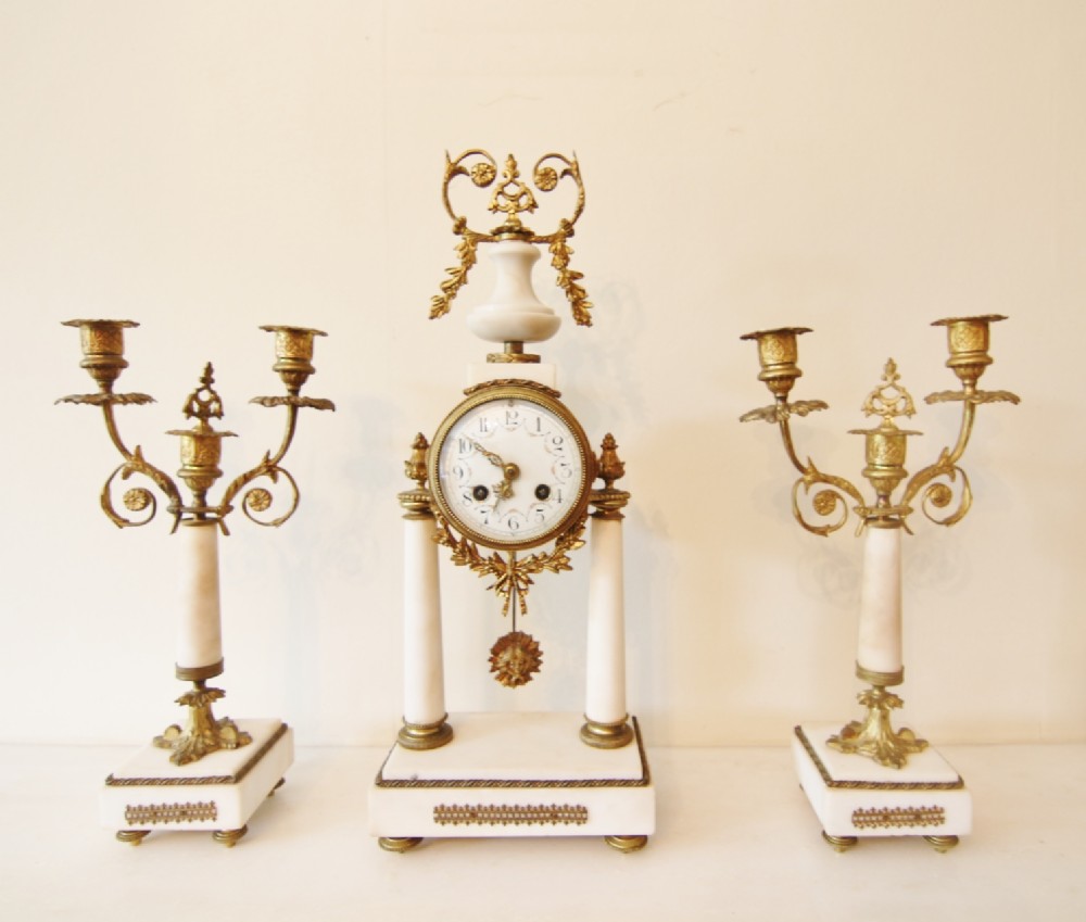 A 19th-century French clock garniture set featuring a white marble portico clock with gilded bronze mounts flanked by two matching candelabras.