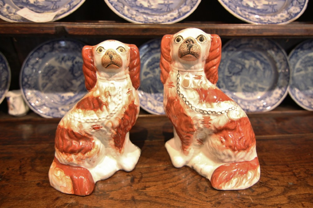 A pair of 19th-century earthenware Staffordshire spaniel figurines painted in terracotta and white with black painted chain collars.