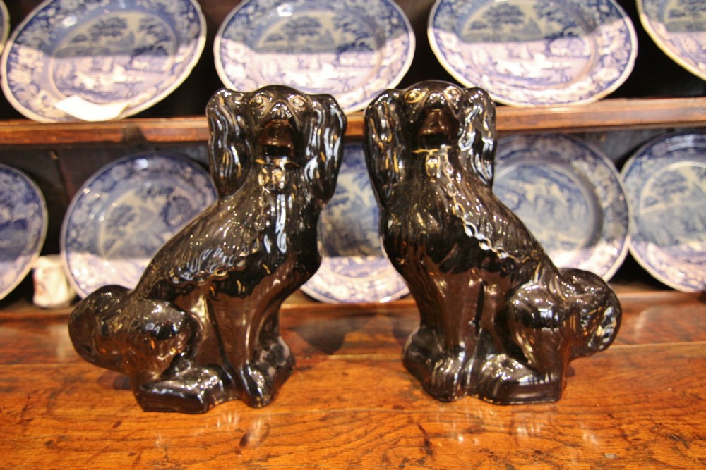 A pair of 19th-century seated ceramic spaniel dogs featuring a high-gloss black glaze and gilded accents.
