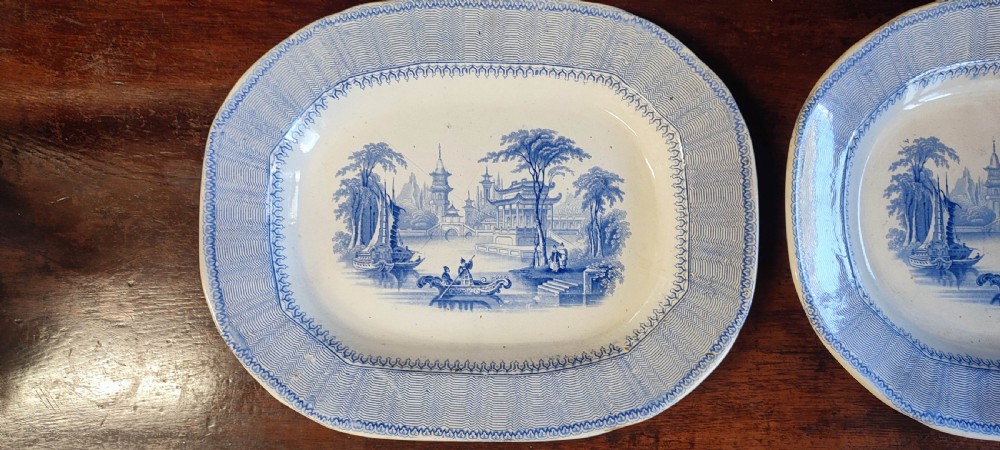 A pair of 19th-century oval earthenware meat dishes featuring blue transfer-printed chinoiserie landscape scenes with pagodas, boats, and detailed geometric borders. View II