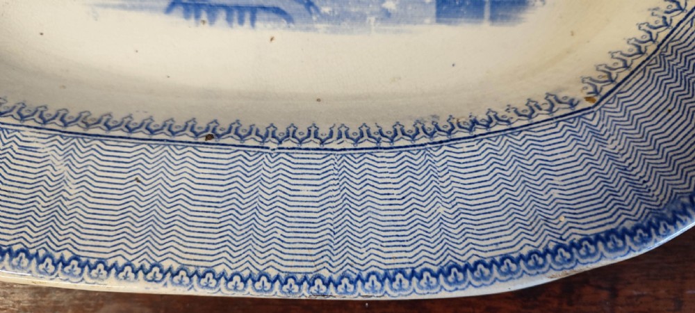 A pair of 19th-century oval earthenware meat dishes featuring blue transfer-printed chinoiserie landscape scenes with pagodas, boats, and detailed geometric borders. View III