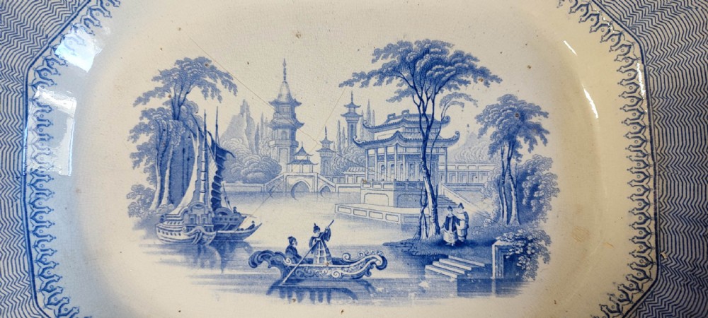 A pair of 19th-century oval earthenware meat dishes featuring blue transfer-printed chinoiserie landscape scenes with pagodas, boats, and detailed geometric borders. View V