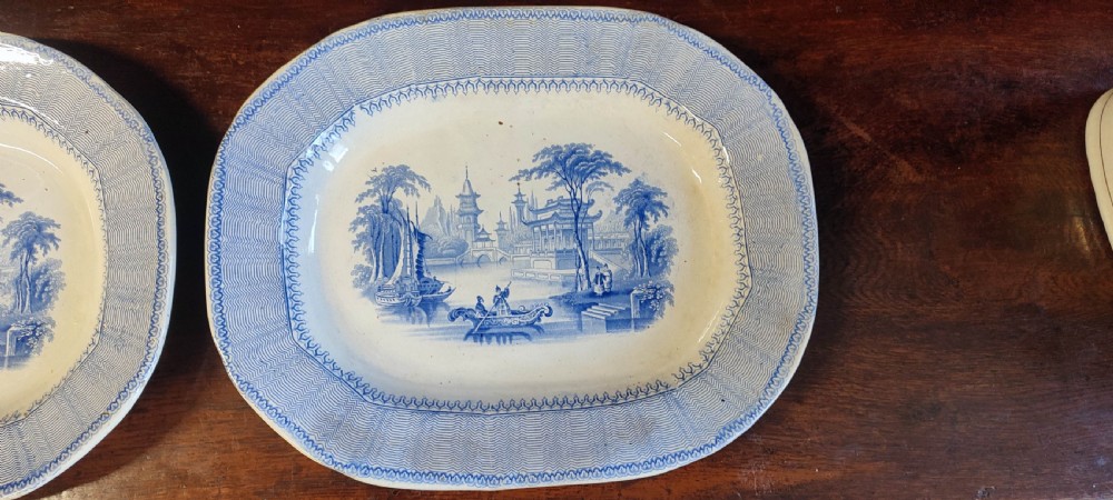 A pair of 19th-century oval earthenware meat dishes featuring blue transfer-printed chinoiserie landscape scenes with pagodas, boats, and detailed geometric borders. View VI