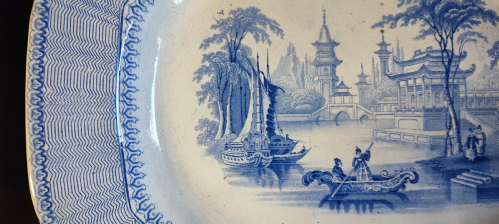 A pair of 19th-century oval earthenware meat dishes featuring blue transfer-printed chinoiserie landscape scenes with pagodas, boats, and detailed geometric borders. View VII