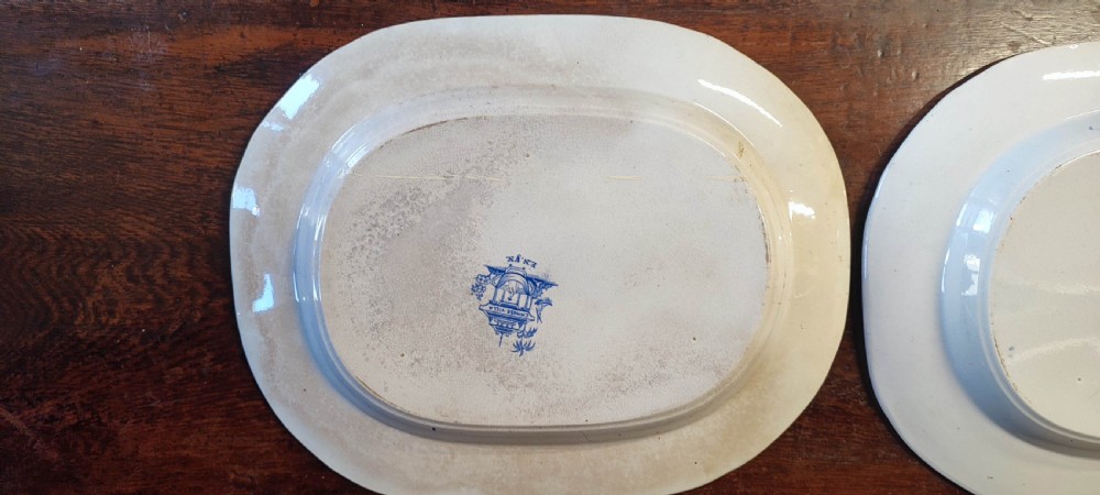 A pair of 19th-century oval earthenware meat dishes featuring blue transfer-printed chinoiserie landscape scenes with pagodas, boats, and detailed geometric borders. View VIII