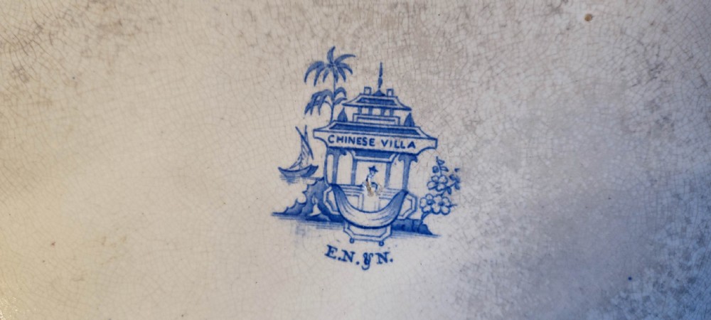 A pair of 19th-century oval earthenware meat dishes featuring blue transfer-printed chinoiserie landscape scenes with pagodas, boats, and detailed geometric borders. View IX