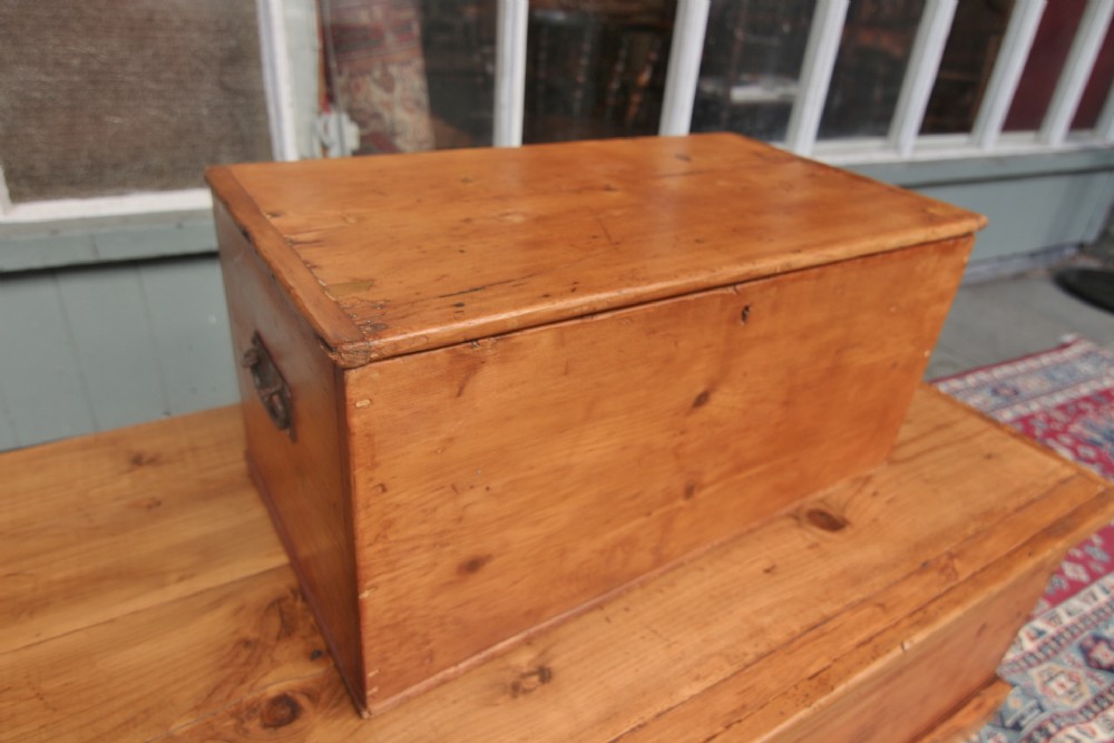 A small 19th-century rectangular pine storage box with a flat top lid, dovetail joinery, and iron side handles.