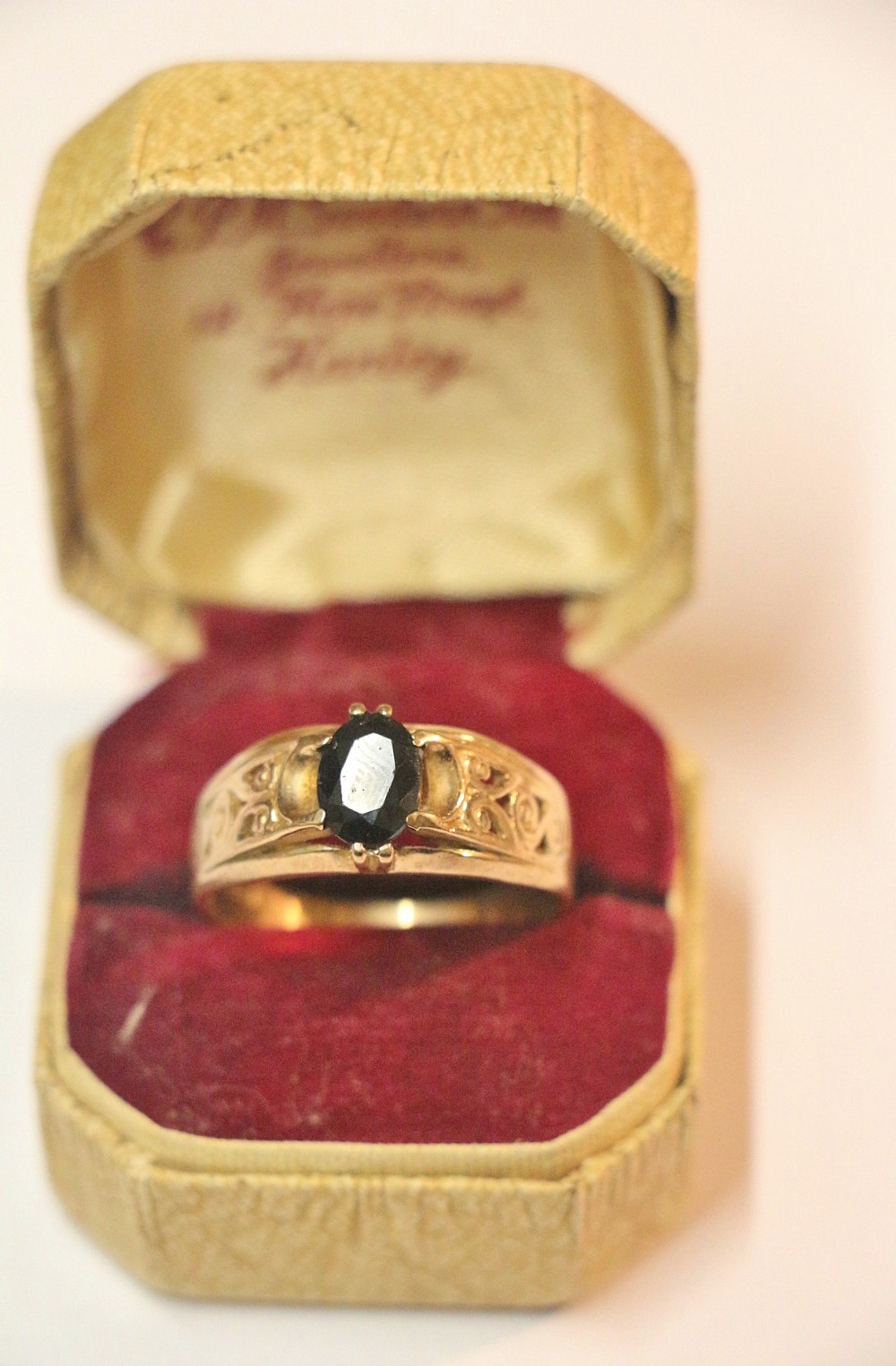 A Victorian 9ct yellow gold ring featuring an oval deep blue sapphire held in a claw setting with carved scroll detail on the shoulders.