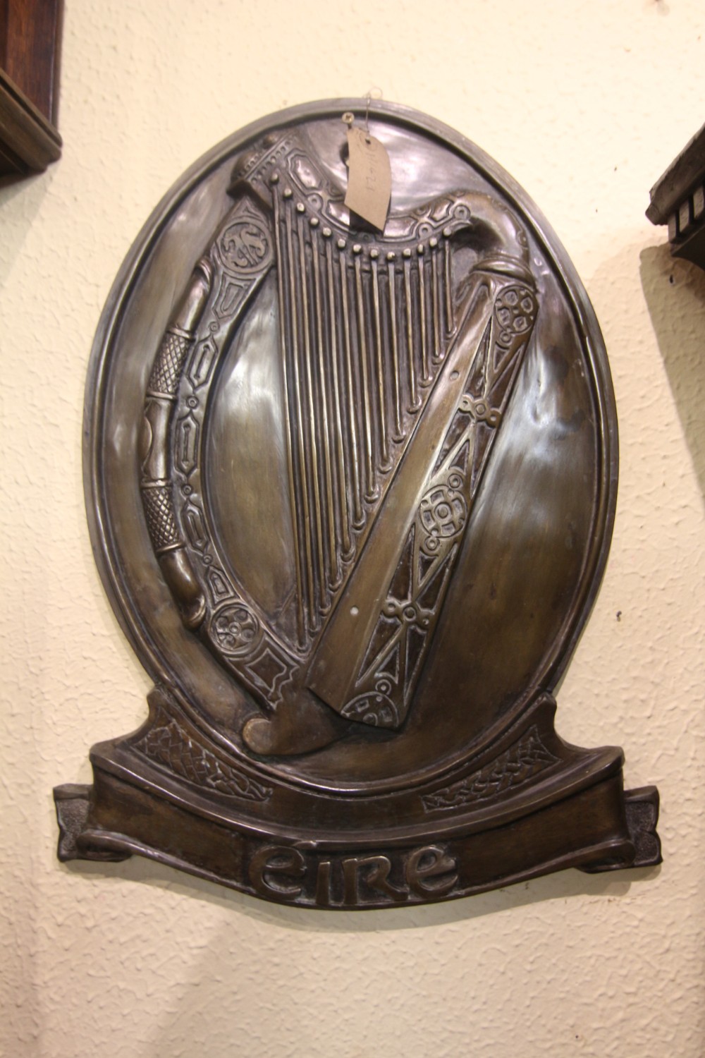 A cast bronze oval wall plaque featuring an Irish harp relief above a scroll banner inscribed with Eire in Gaelic typography.
